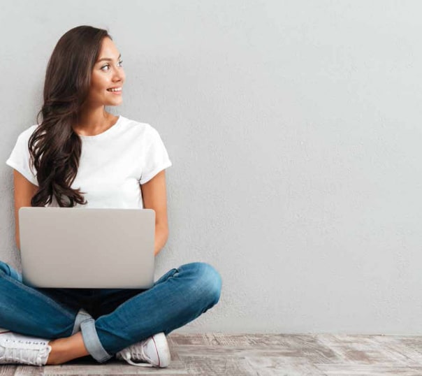 Junge Frau mit Laptop sitzt vor einer grauen Wand